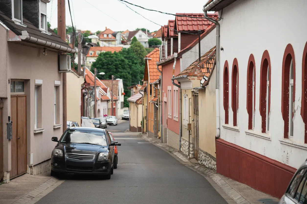 This is a narrow alley in a European street, with a shabby black car parked on the road.