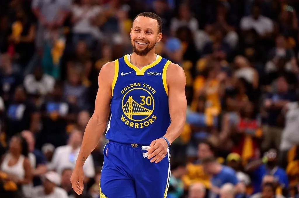 On the court, NBA basketball star Stephen Curry is walking forward in a blue jersey.